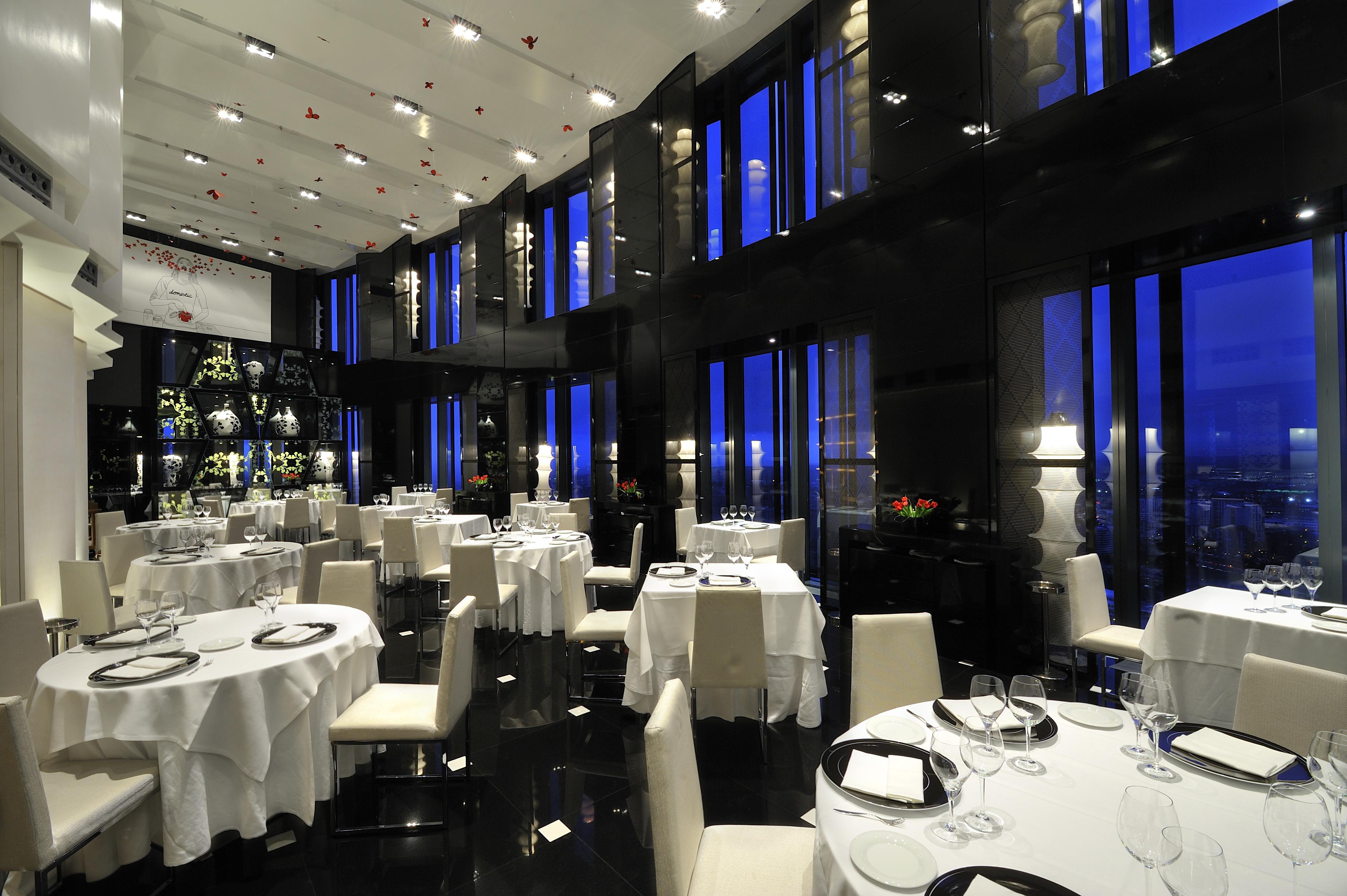 Eurostars Madrid Tower Hotell Eksteriør bilde The photo shows an elegant restaurant interior, characterized by its modern design and luxurious ambiance. The space features several round dining tables, each set with white tablecloths and tableware, including wine glasses. The walls are made of da