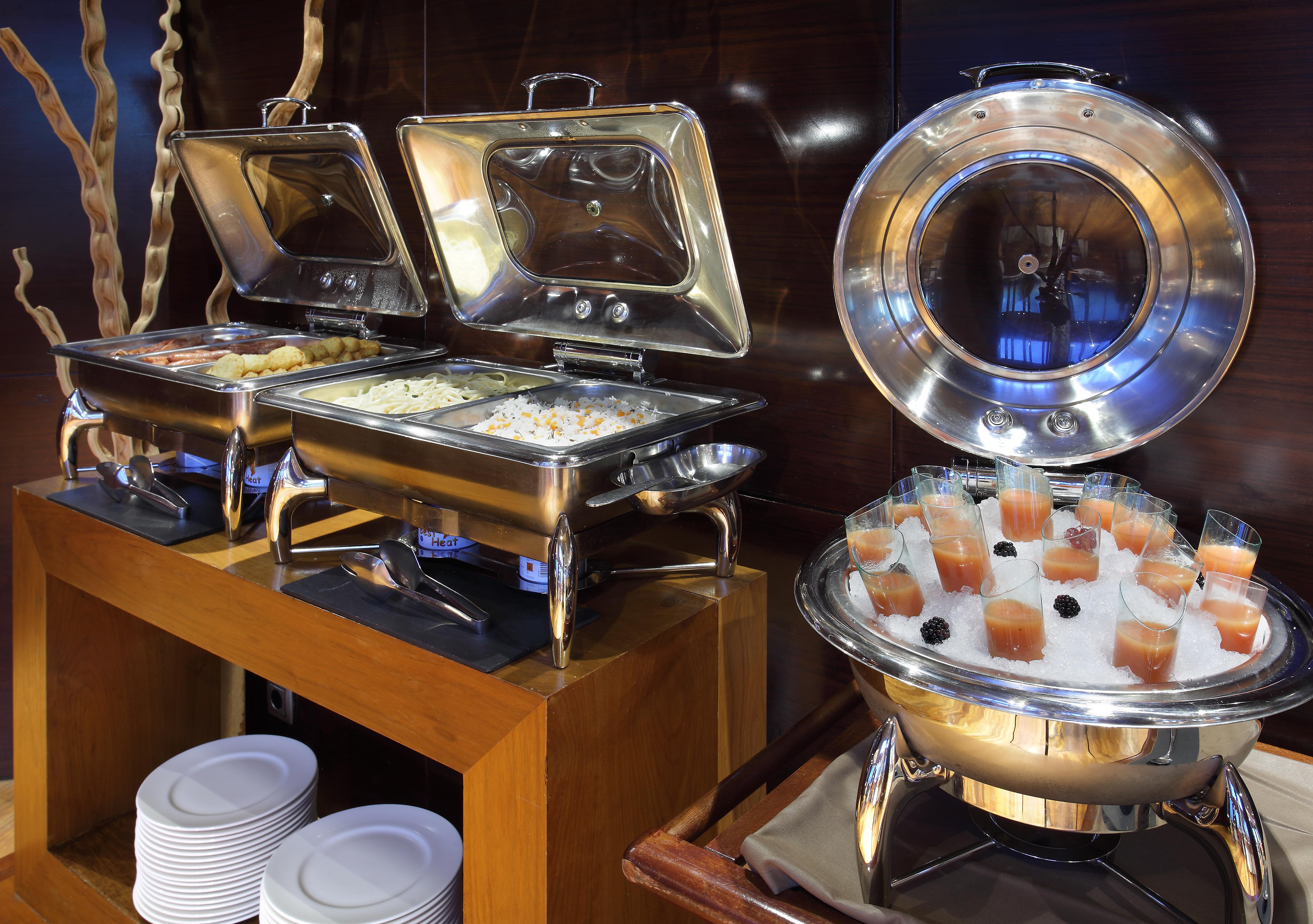 Eurostars Madrid Tower Hotell Eksteriør bilde The photo shows a buffet setup with several food items. On the left, there are two stainless steel chafing dishes, each containing food, possibly rice or a similar dish. On the right, there is a round chafing dish that holds small cups or glasses fil