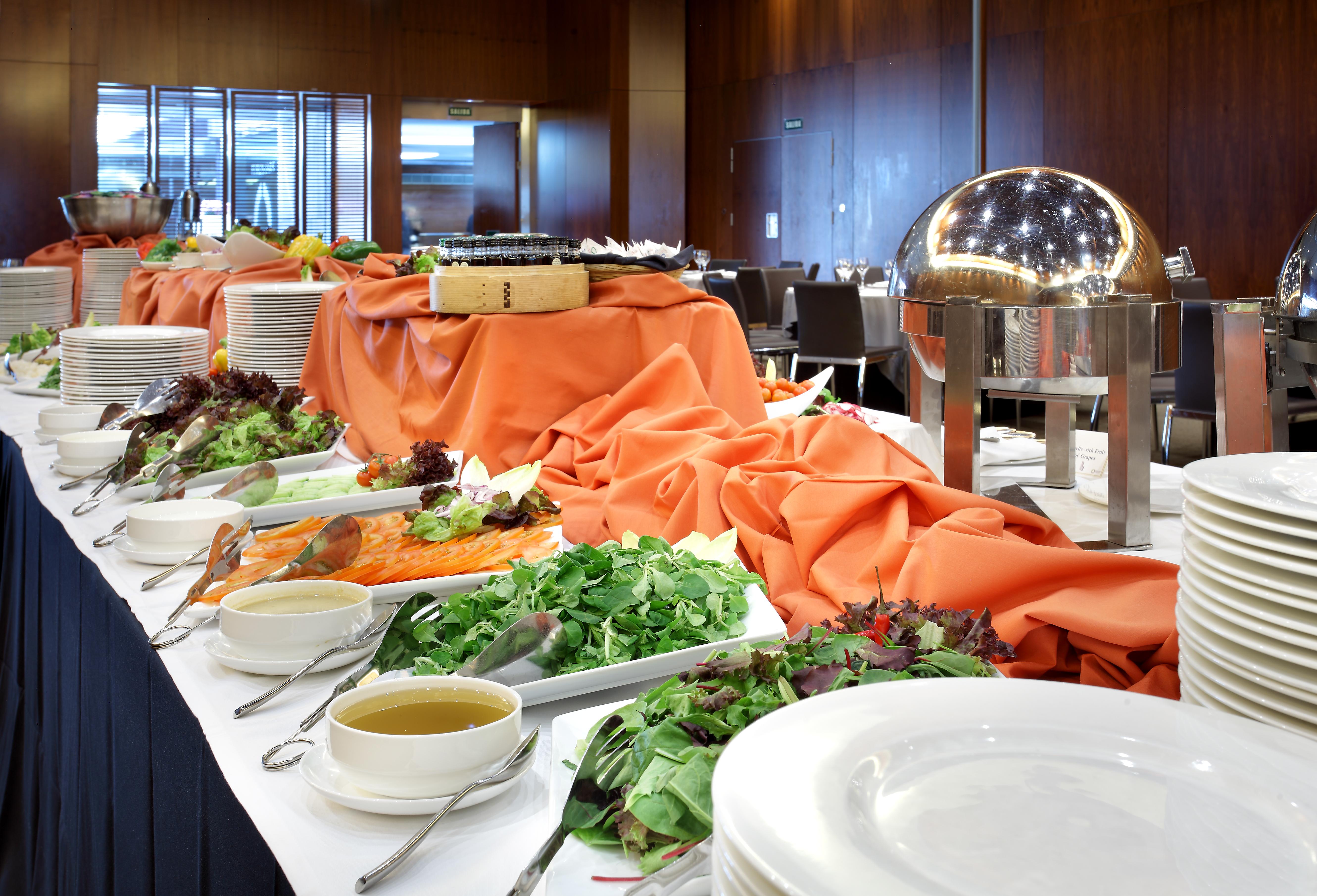 Eurostars Madrid Tower Hotell Eksteriør bilde The photo shows a buffet table set up for a meal. The table is covered with an orange cloth and features a variety of food items. There are platters of greens and salads, as well as bowls of soup or dressing. A metal chafing dish is present, likely c