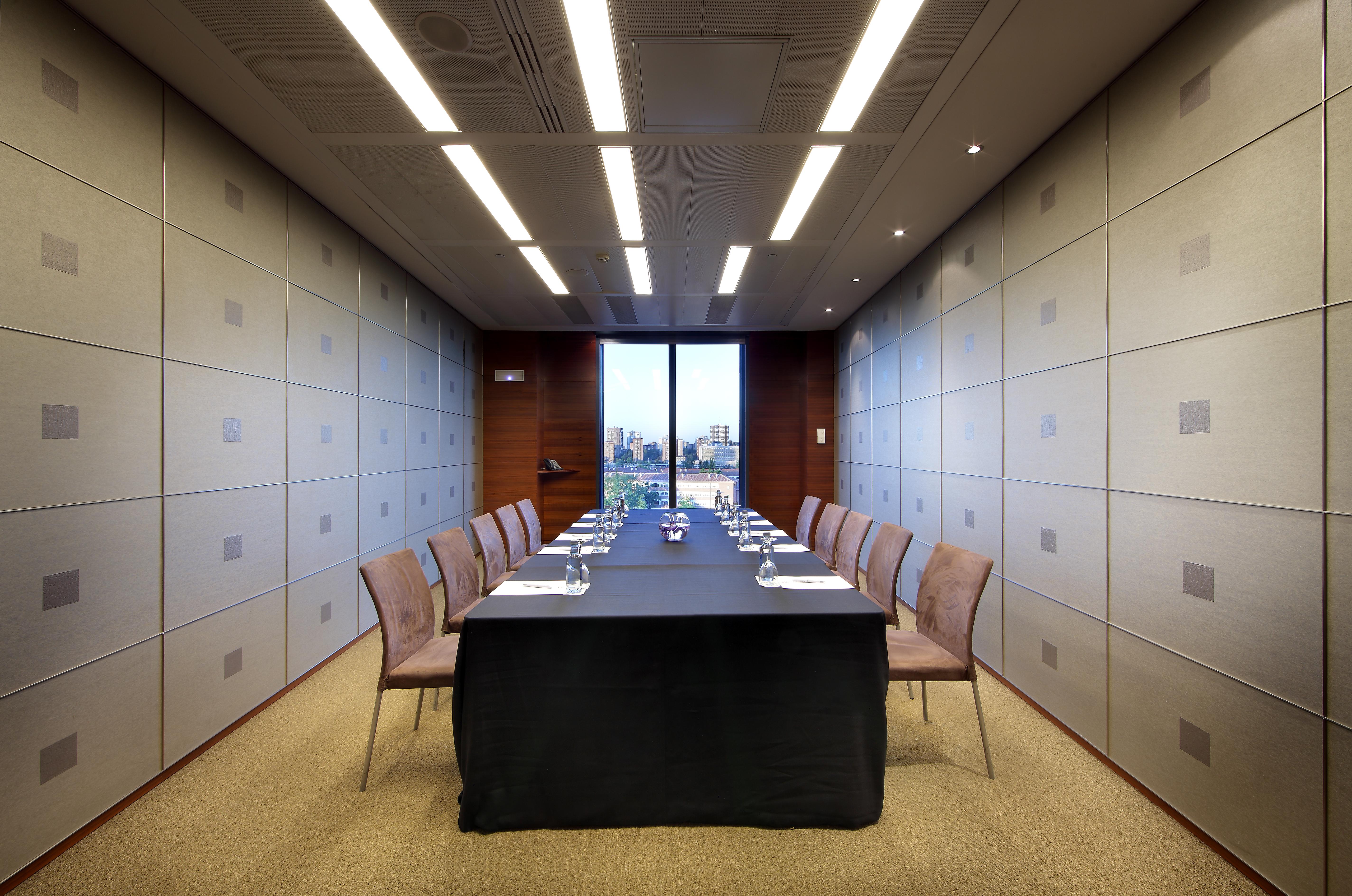Eurostars Madrid Tower Hotell Eksteriør bilde The photo shows a modern conference room. In the center, there is a long table covered with a black tablecloth. Surrounding the table are several chairs arranged neatly. The walls have a sleek design with light-colored panels, and overhead, there are