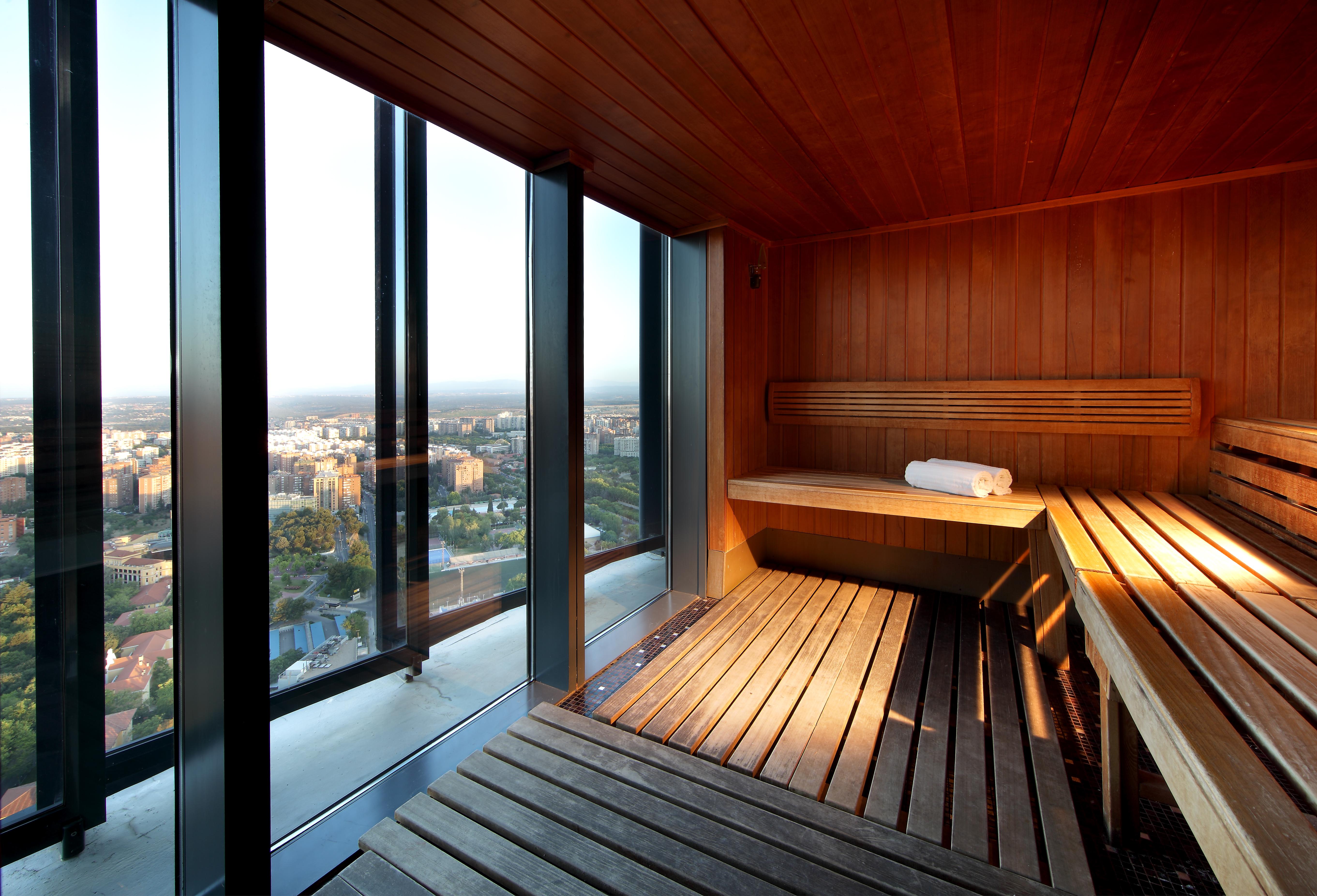 Eurostars Madrid Tower Hotell Eksteriør bilde The image shows a modern sauna with wooden interiors. The sauna features benches made of wood, providing a relaxing space. One of the benches has a rolled towel resting on it. Large glass windows allow for a panoramic view of the outside, showcasing 