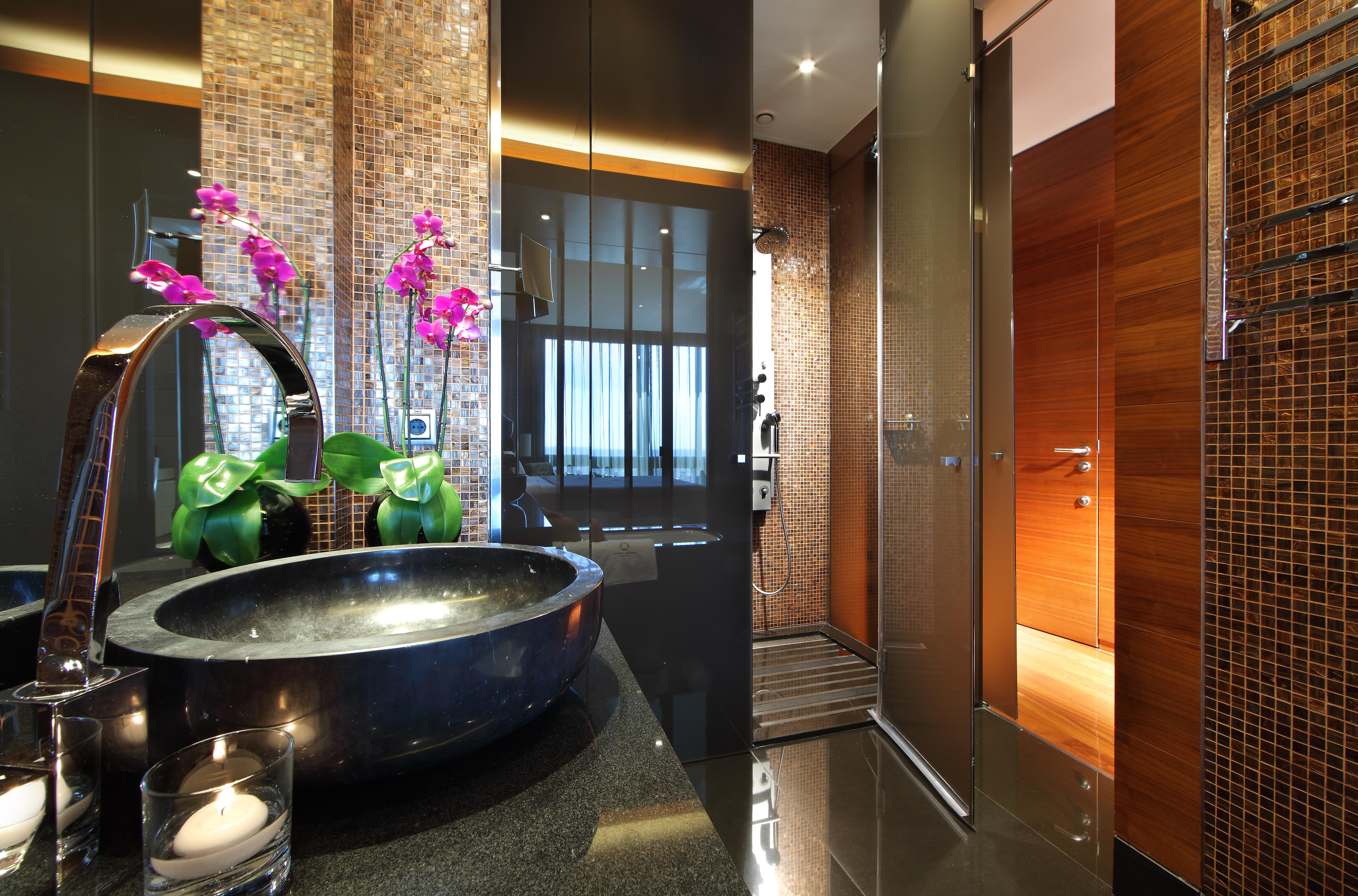 Eurostars Madrid Tower Hotell Eksteriør bilde The photo shows a modern and stylish bathroom. On the left, there is a sleek black basin set on a dark countertop, adorned with decorative elements such as a candle and potted green plants. To the side, there are elegant pink orchids adding a pop of 