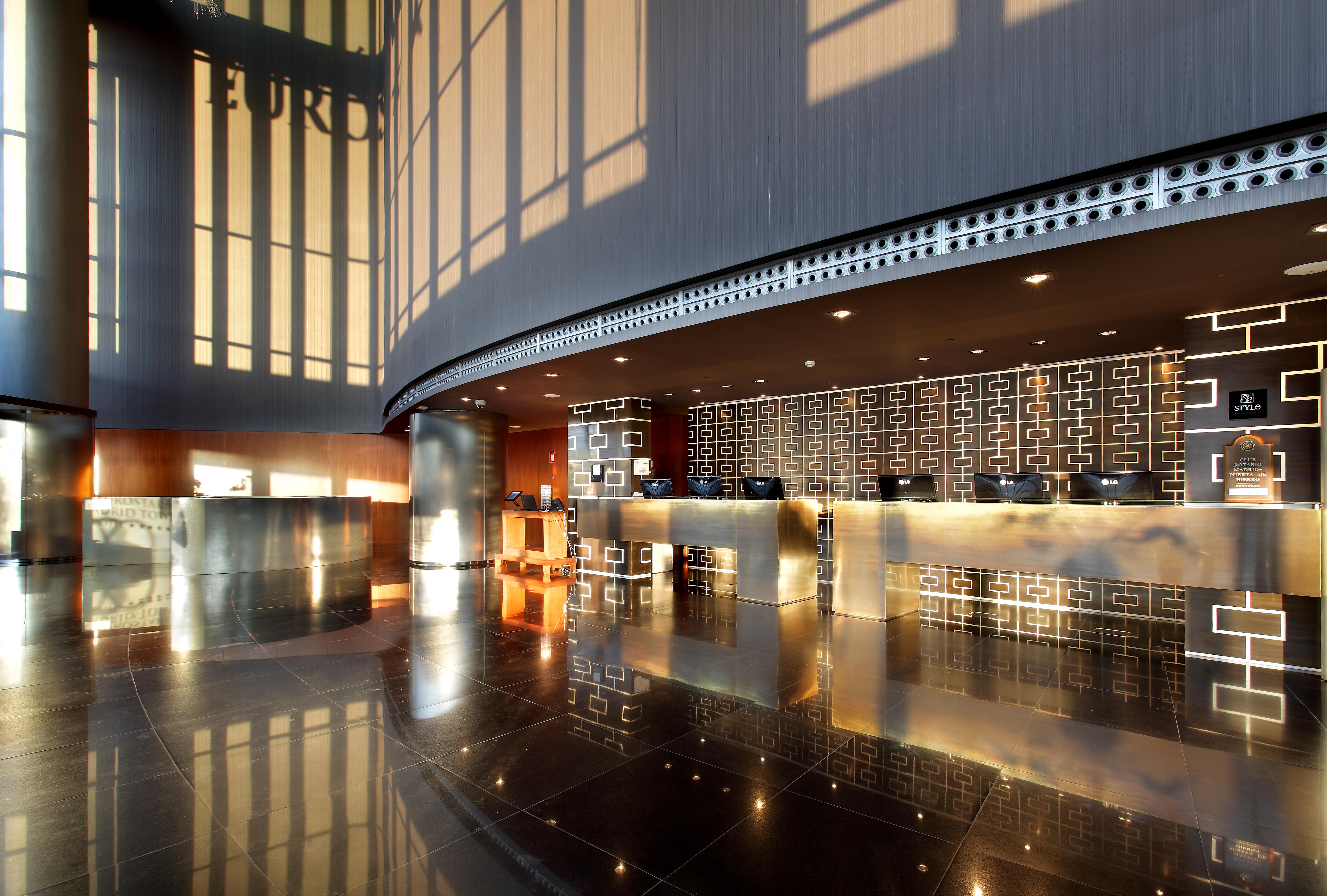 Eurostars Madrid Tower Hotell Eksteriør bilde The photo shows the interior of a modern hotel lobby. It features a sleek reception desk with a polished surface and an elegant design. The lobby has large windows allowing natural light to flood in, creating a bright and inviting atmosphere. The flo