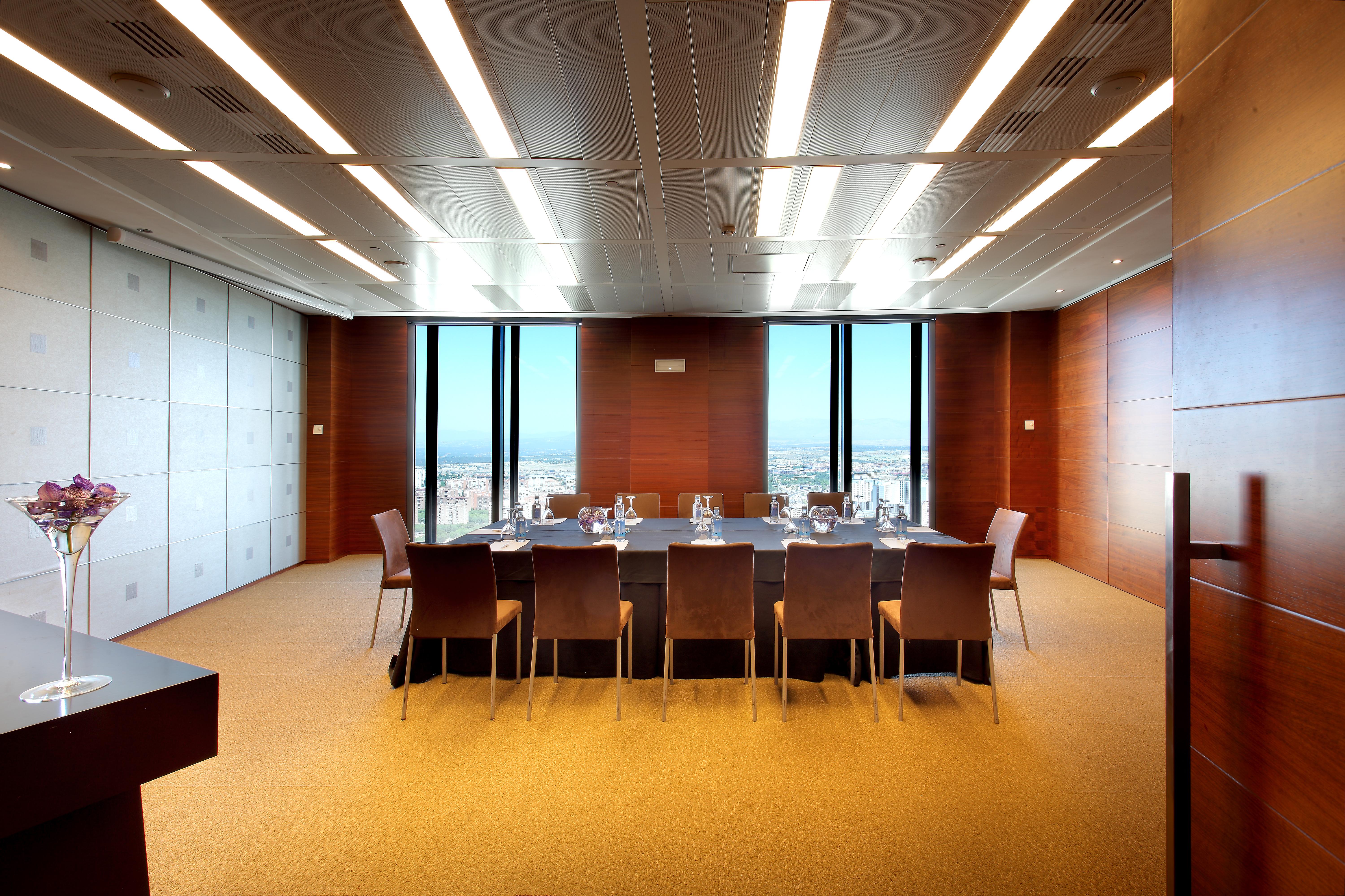 Eurostars Madrid Tower Hotell Eksteriør bilde The photo shows a modern conference room or meeting space. It features a large rectangular table surrounded by several leather chairs. The room has wooden paneling and large windows that let in natural light, providing a view of the outside landscape