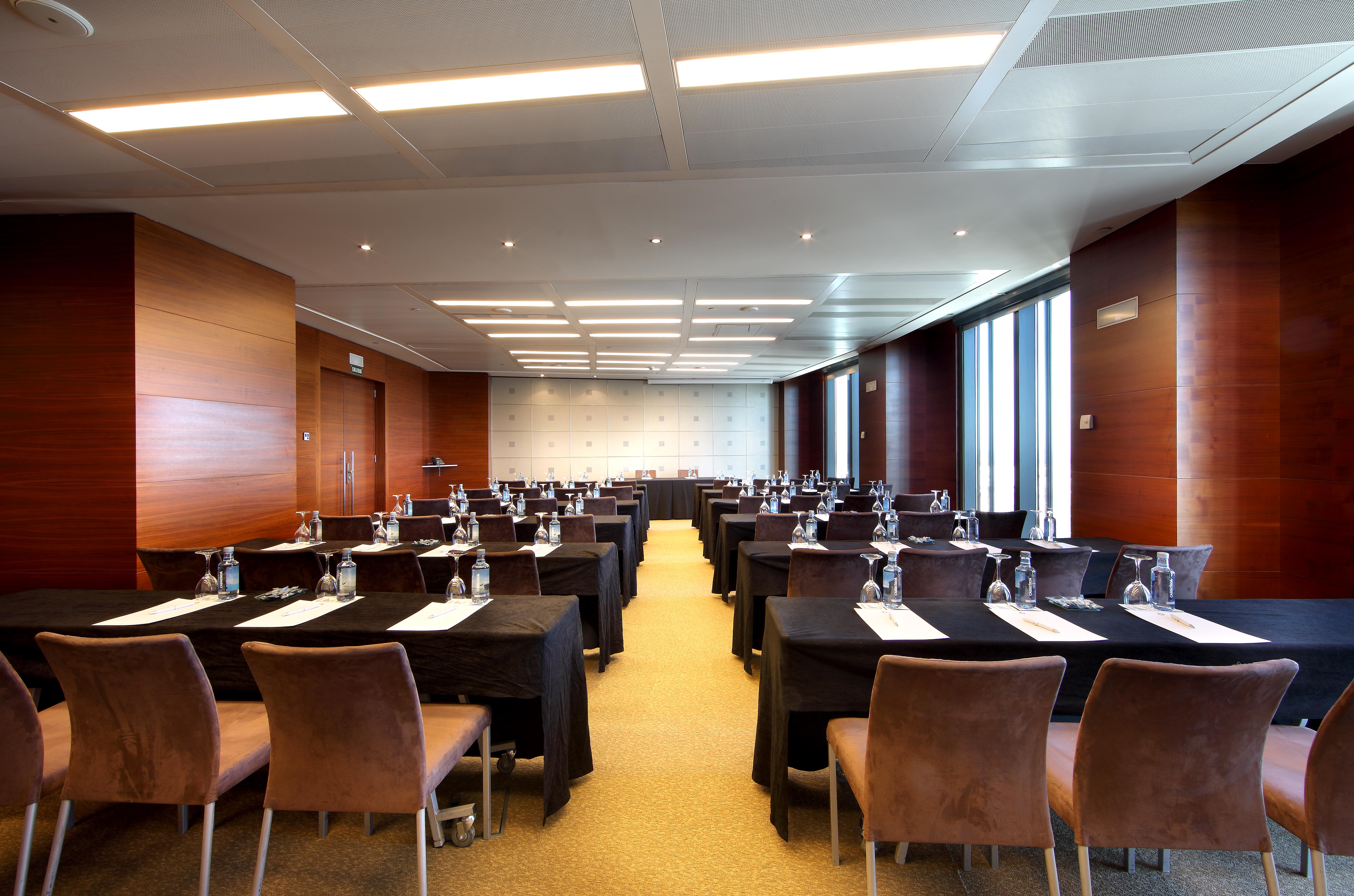 Eurostars Madrid Tower Hotell Eksteriør bilde The photo shows a modern conference room set up for a meeting or seminar. There are multiple tables arranged in rows, each covered with black tablecloths. Each table has a clean white sheet, and water bottles are placed at each setting. The room is w