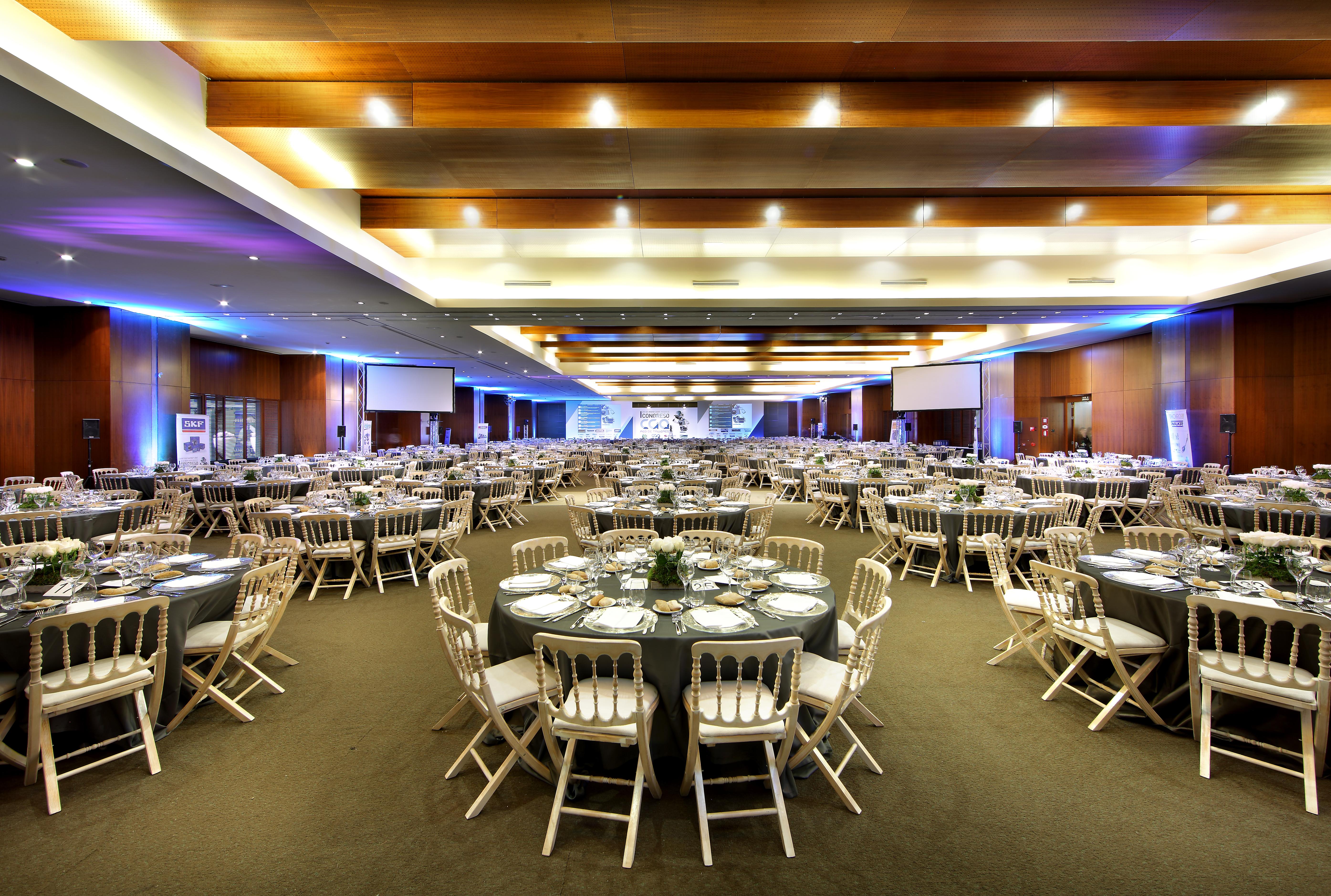 Eurostars Madrid Tower Hotell Eksteriør bilde The photo shows a large banquet hall set up for an event. The room is filled with numerous round tables, each adorned with dark tablecloths and decorative centerpieces. There are white chairs arranged around the tables. The lighting is soft, with a c