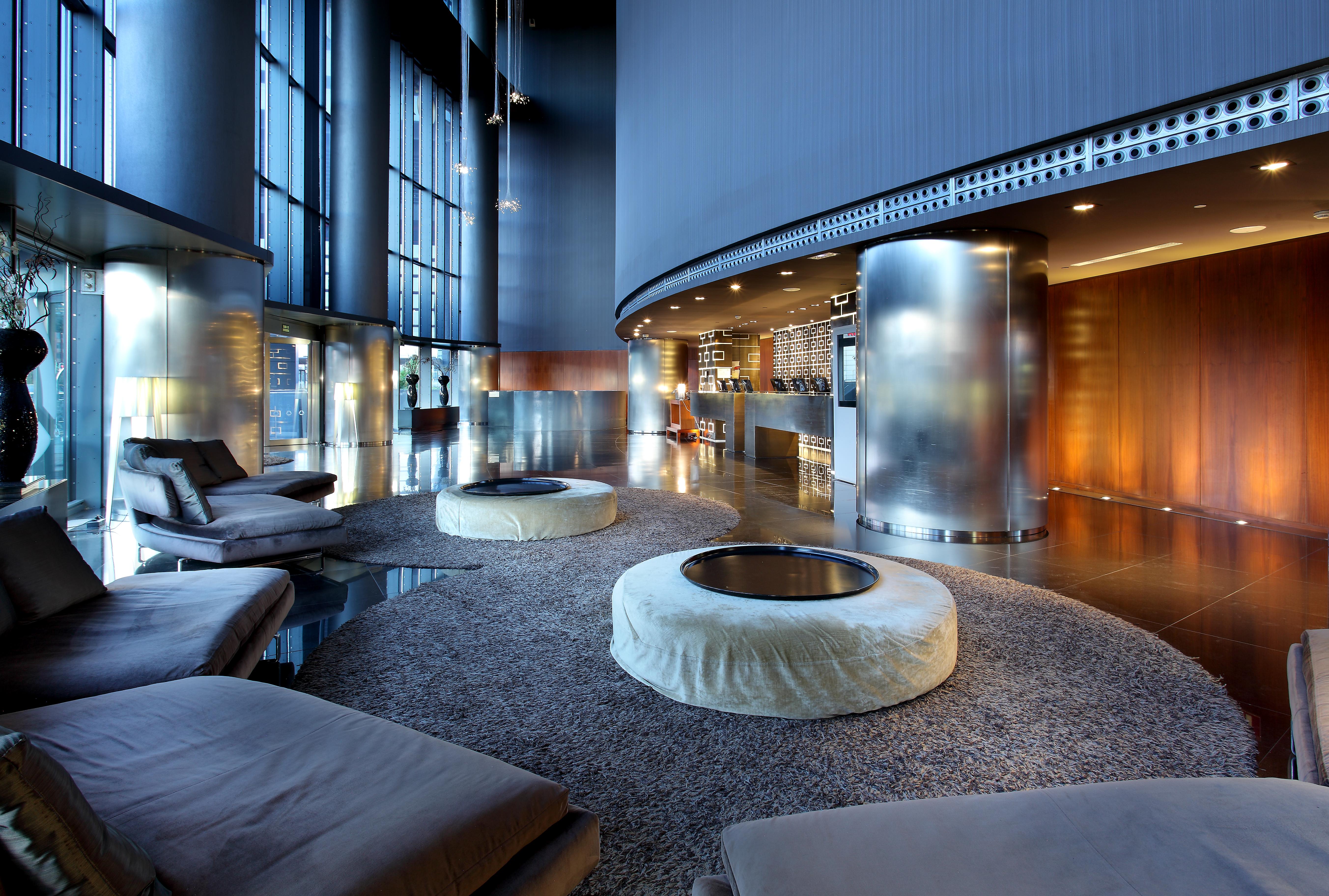 Eurostars Madrid Tower Hotell Eksteriør bilde The photo depicts a modern and stylish lounge area. The space features light-filled windows that allow for ample natural light, creating an airy atmosphere. There are several circular seating arrangements with plush, low-slung cushions arranged aroun