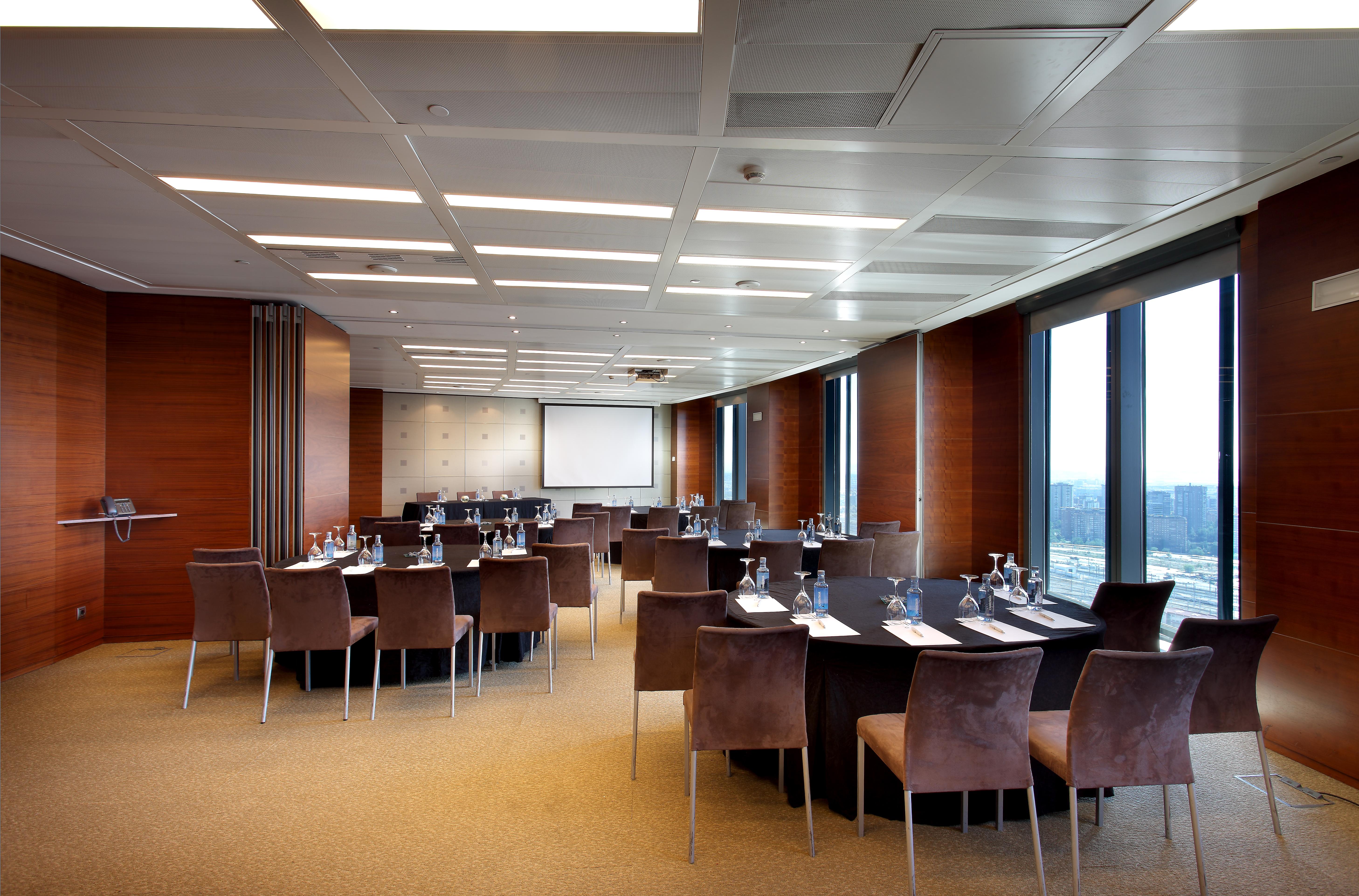 Eurostars Madrid Tower Hotell Eksteriør bilde The photo shows a modern conference room set up for a meeting or event. The room features a large, rectangular table surrounded by upholstered chairs. Each place at the table has a notepad and pen, and there are glasses of water provided. Large windo