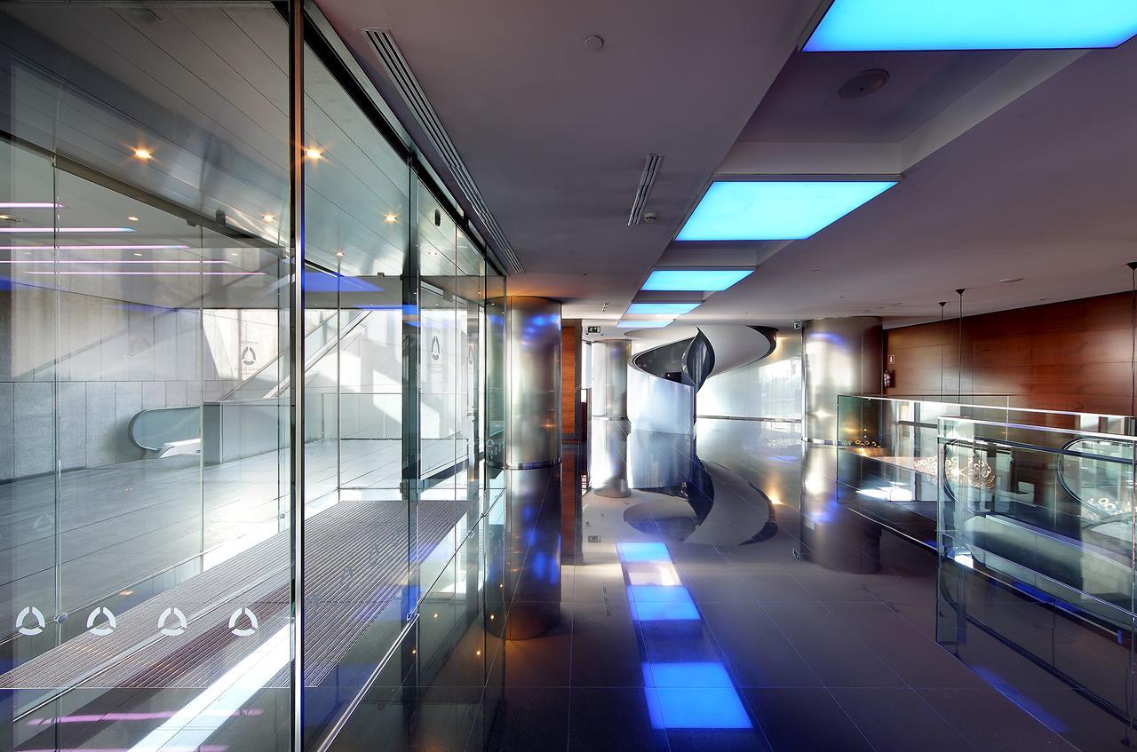 Eurostars Madrid Tower Hotell Eksteriør bilde The photo shows a modern, sleek interior space characterized by large glass walls and reflective surfaces. The ceiling features blue-lit sections, creating a contemporary atmosphere. The polished floor enhances the overall brightness of the area, and