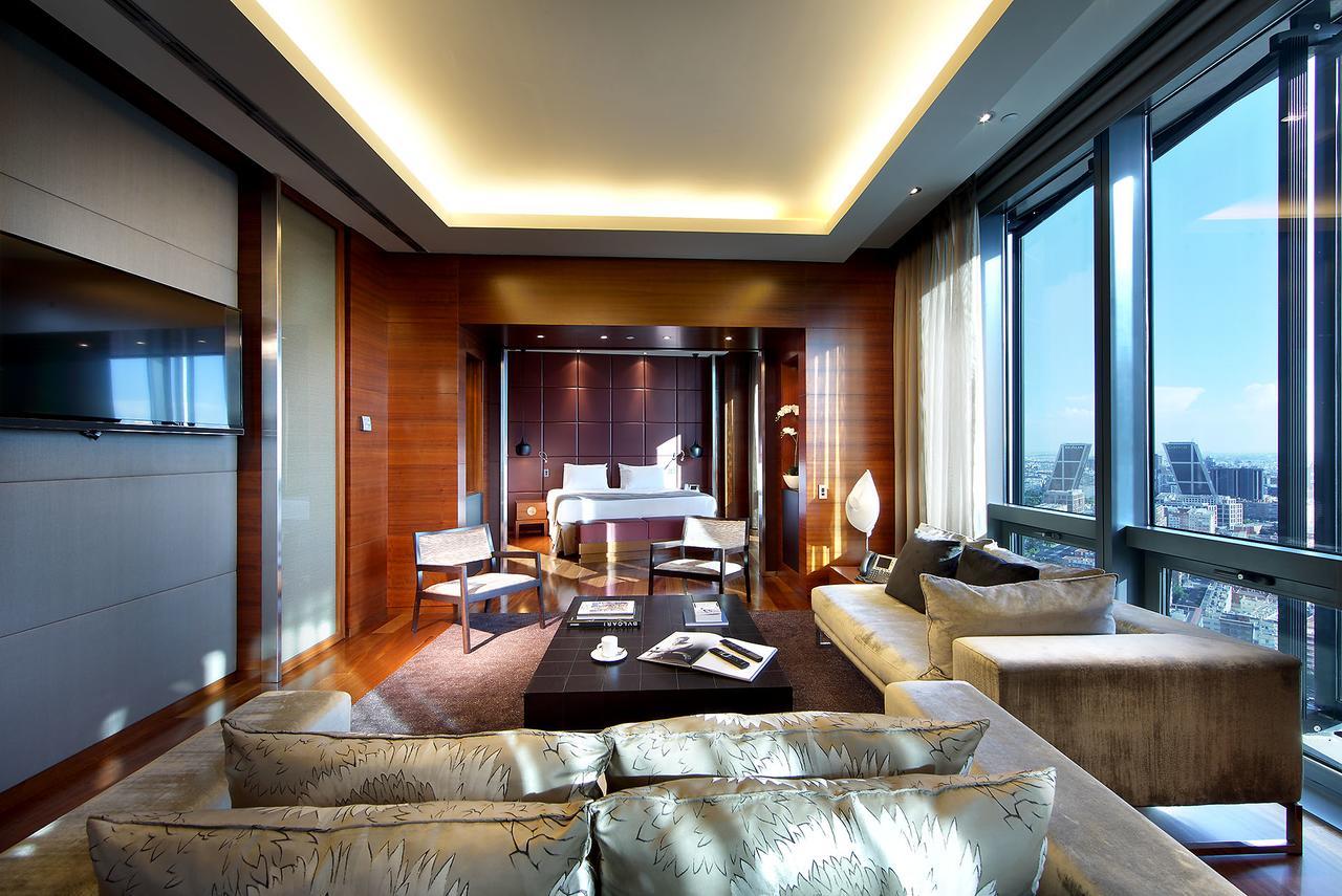 Eurostars Madrid Tower Hotell Eksteriør bilde The photo shows a luxurious hotel room or suite with a modern design. It features large windows that offer a view of the outside, letting in plenty of natural light. The interior has warm wooden accents on the walls and sophisticated lighting through