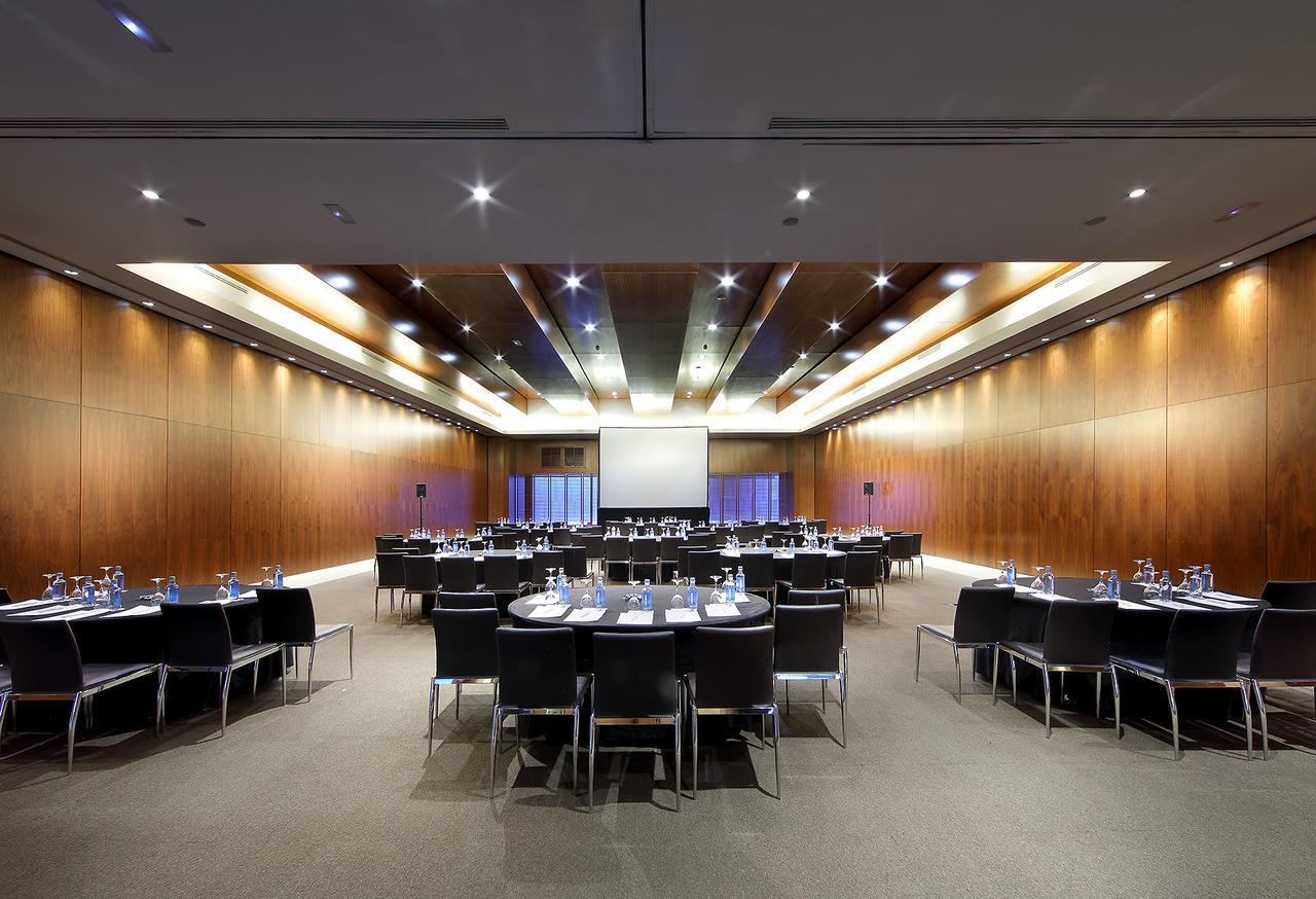 Eurostars Madrid Tower Hotell Eksteriør bilde The photo shows a spacious and modern conference room set up for a meeting or event. There are several round tables arranged in a semi-circle, each covered with a white tablecloth and equipped with water glasses, writing pads, and pens. The room feat