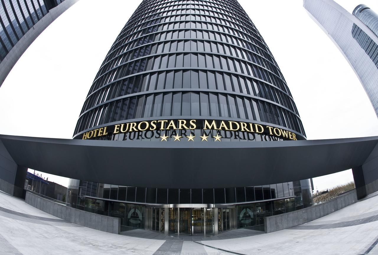 Eurostars Madrid Tower Hotell Eksteriør bilde The photo shows a tall, modern glass building that serves as the Eurostars Madrid Tower Hotel. The building features a sleek, curved design with a prominent entrance. Above the entrance, the hotel's name is displayed in large golden letters, indicati