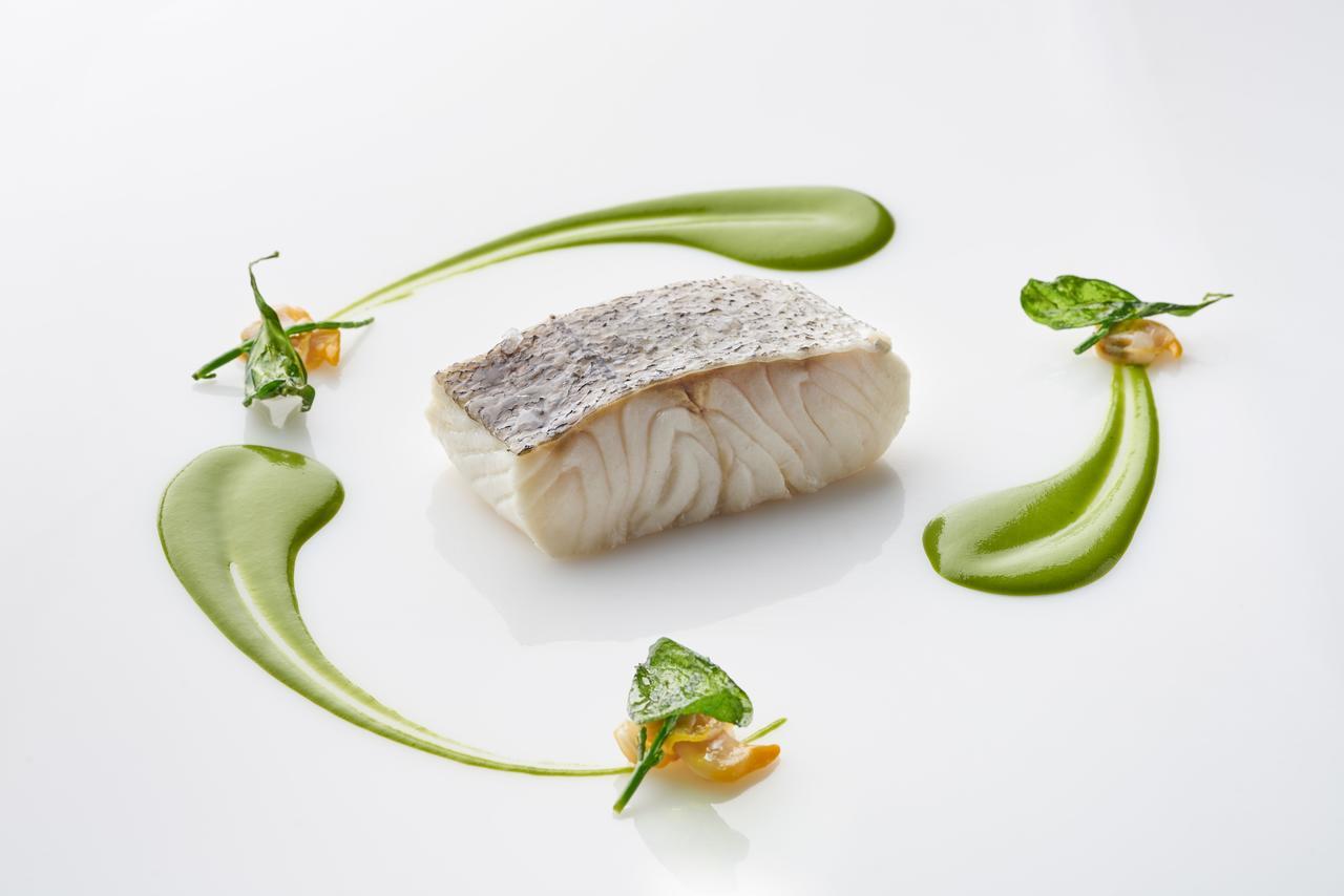 Eurostars Madrid Tower Hotell Eksteriør bilde The photo shows a beautifully presented dish featuring a piece of fish, likely a white fish, with a prominent skin side on top. It is surrounded by artistic garnishes, including vibrant green sauces and small sprigs of herbs. The composition is elega