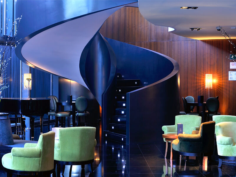 Eurostars Madrid Tower Hotell Eksteriør bilde The photo depicts a stylish and modern interior, likely of a bar or lounge. The focal point is a unique spiral staircase that has a sleek, flowing design, leading to another level. The surrounding area features a combination of dark wood panels and g