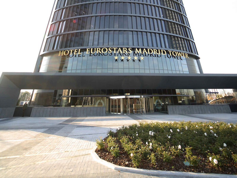 Eurostars Madrid Tower Hotell Eksteriør bilde The photo shows the exterior of the Eurostars Madrid Tower Hotel, which is a modern, high-rise building. The hotel features a sleek glass facade and has "HOTEL EUROSTARS MADRID TOWER" prominently displayed in gold lettering above the entrance. The ar